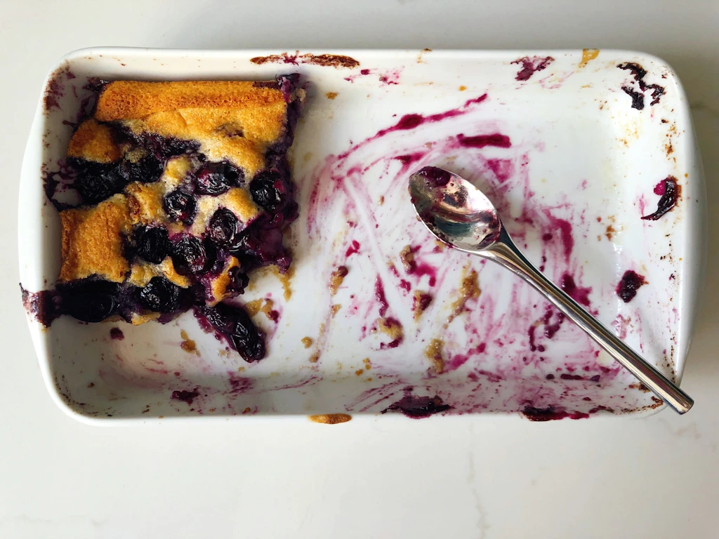 Mostly eaten white dish of blueberry cobbler with small spoon