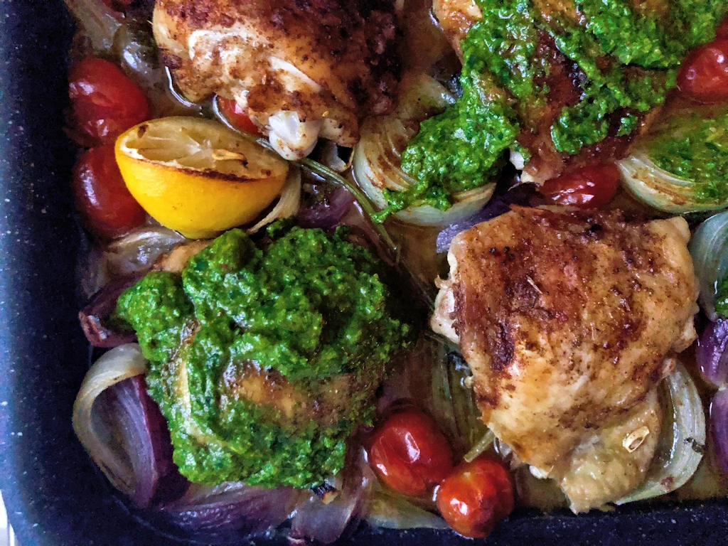 Tray with chicken thighs with bright green sauce chermoula