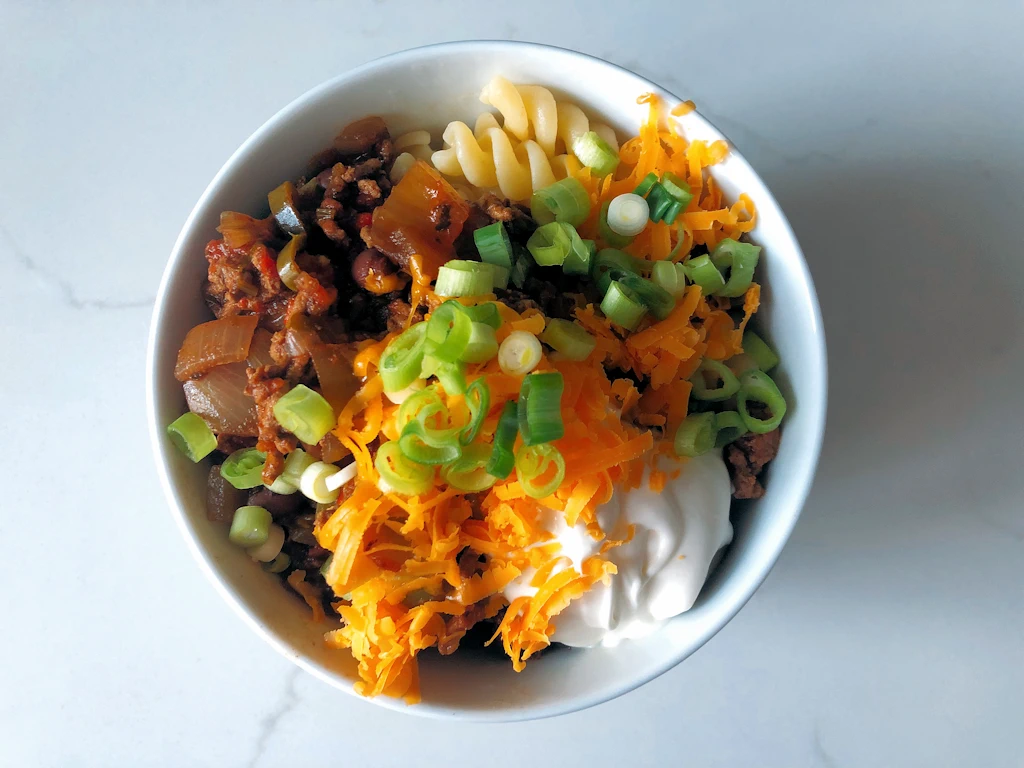 Bowl of chili con carne loaded with cheese, green onions and sour cream