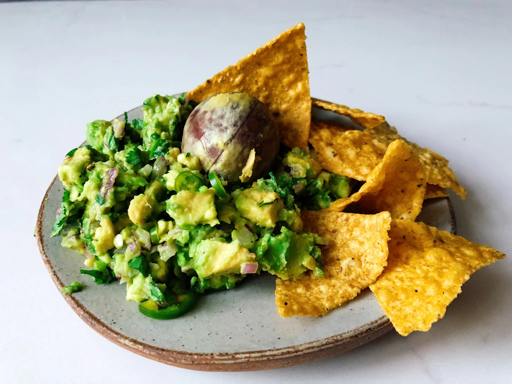 Plate with fresh guacamole with avacado pit and tortilla chips