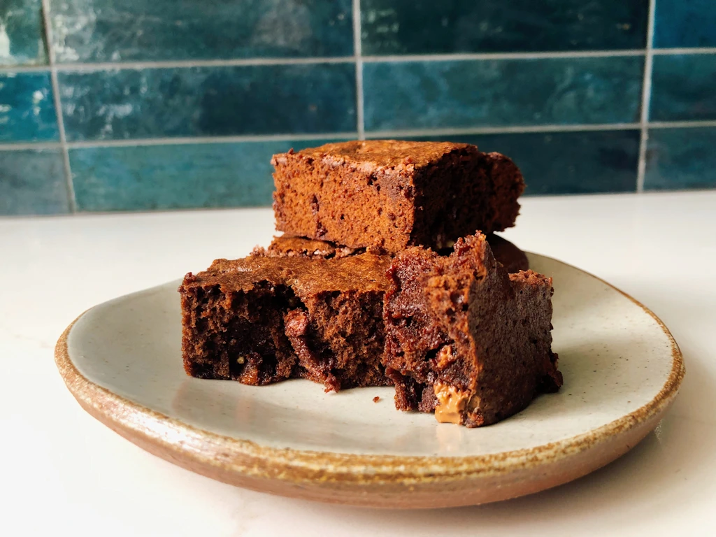 Plate of icing sugar brownies on counter with blue tile background