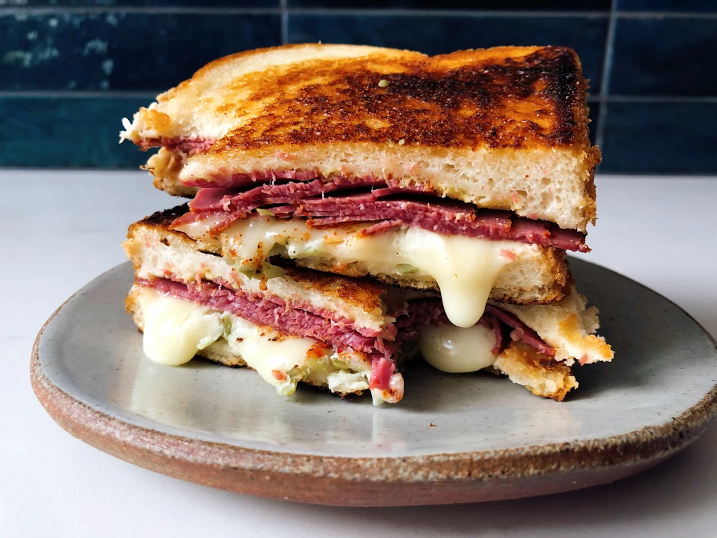 Two halves of a pastrami taleggio pickle sandwich stacked on a plate