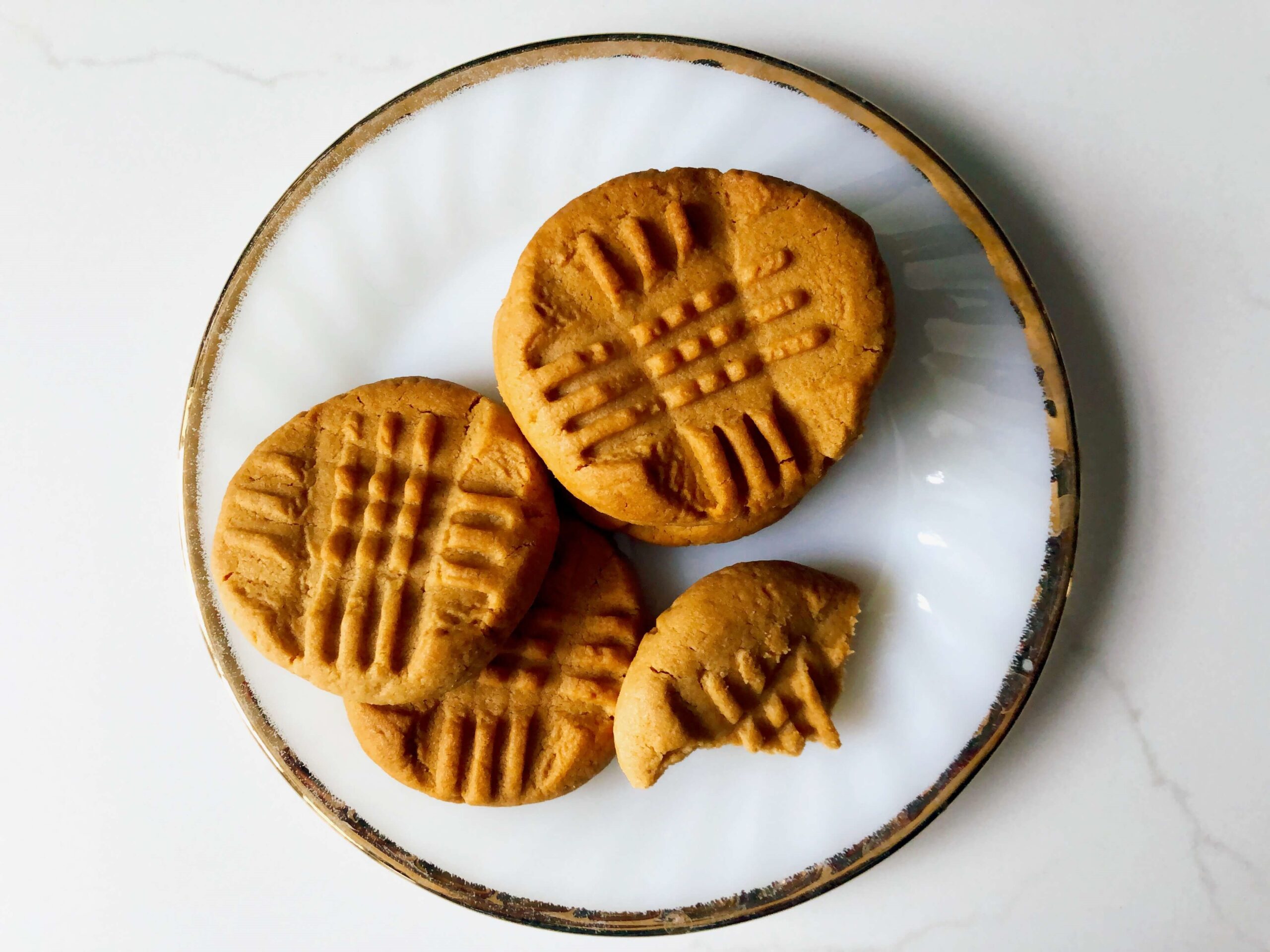 Three and a half peanut butter cookies on a round plate with a gold rim.