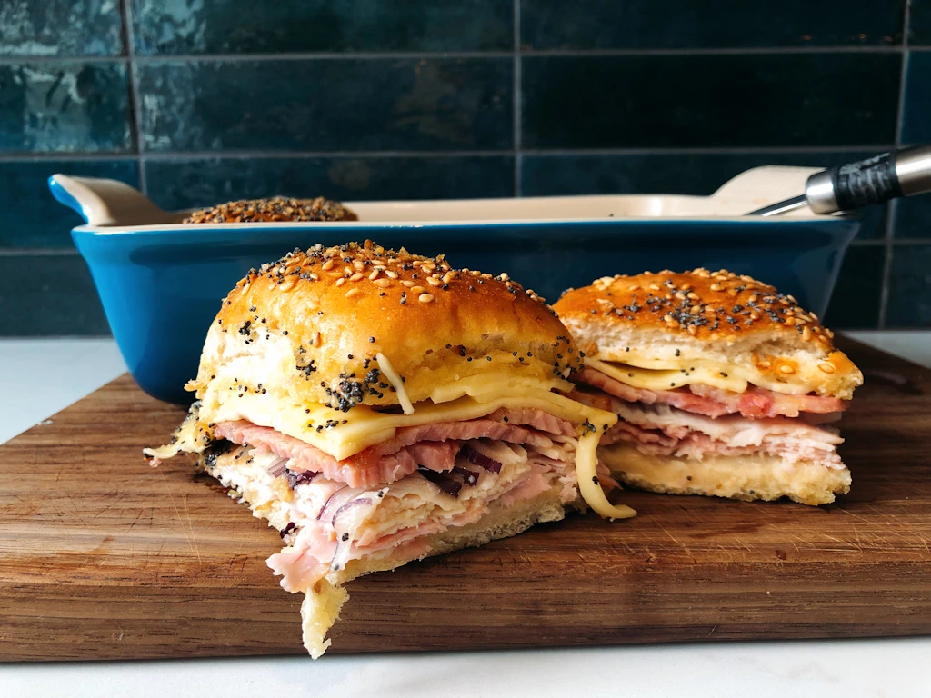 Cutting board with one and a half chicken club sliders in front of the baking dish