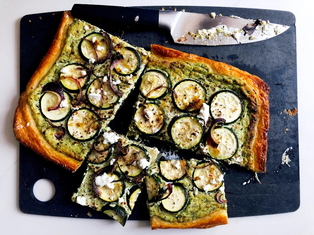 Overhead shot of courgette pesto flatbread on a cutting board with knife