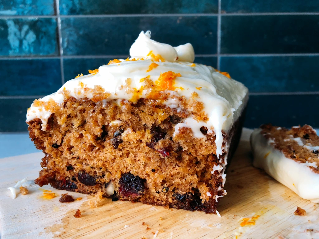 Cutting board with cranberry orange parsnip cake with cream cheese frosting