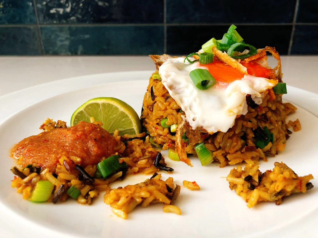 Plate with a scoop of nasi goreng with a fried egg on top with sambal and a lime on the side