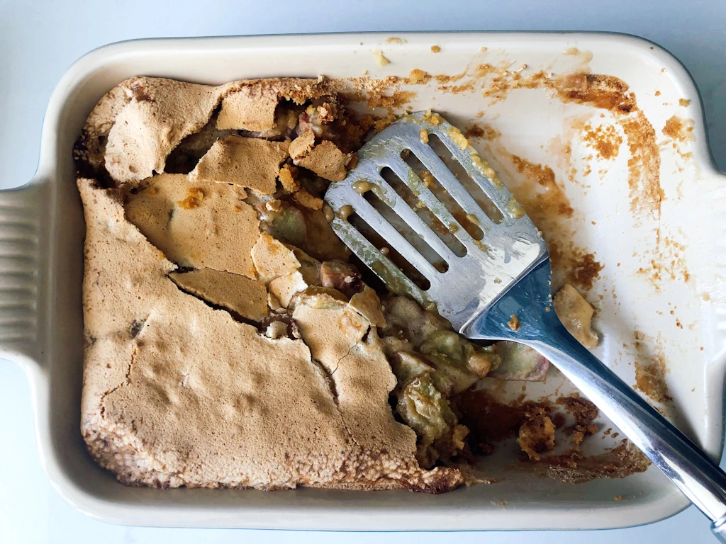 Baking pan of rhubarb dream dessert half eaten with spatula.