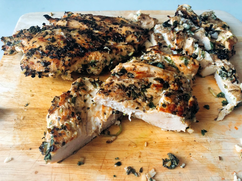 Cutting board with three flattened spicy chicken breasts on it.