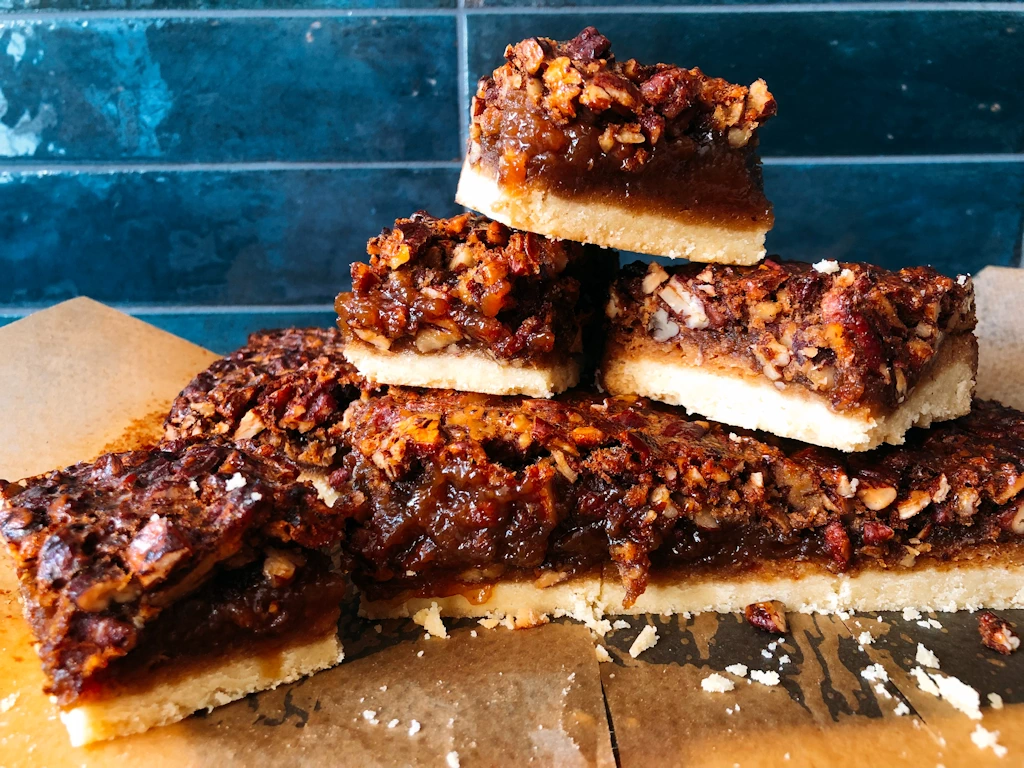 Recipe for Pecan Pie Bars stacked up against a blue background